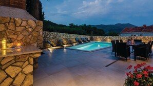 A stone wall, a pool, lounge chairs, a dining table with chairs, and a view of mountains. - Zaton Family Getaway near Adriatic Sea (Zaton)