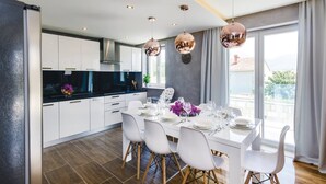 A modern kitchen with white cabinets, a black countertop, and a dining area with a white table set for four. - Zaton Family Getaway near Adriatic Sea (Zaton)