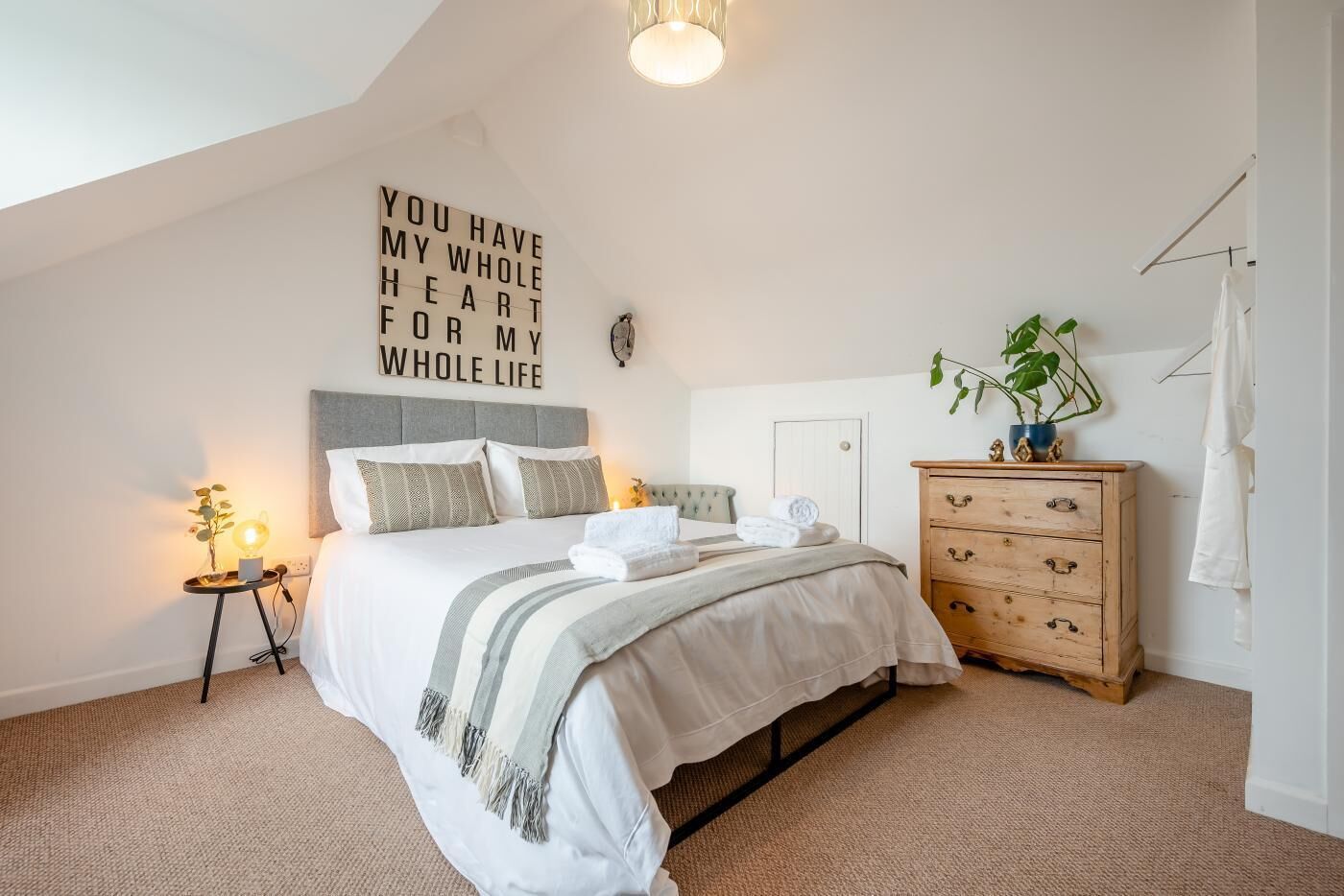 A bedroom with a bed, bedside table, dresser, and a wall with a motivational quote.