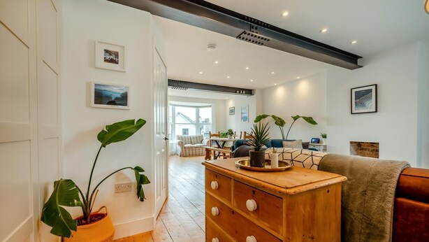 A spacious living room with a wooden dresser, a large potted plant, and a cozy seating area with a sofa and armchairs. - 3 Bed in Bude (oc-t30908) (Bude)