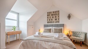 A bedroom with a bed, a bedside table, a chair, a wall with a message, and a window. - 3 Bed in Bude (oc-t30908) (Bude)