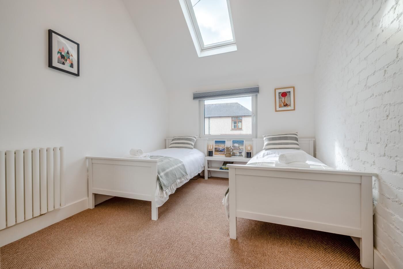A bedroom with two beds, a skylight, a radiator, and a white brick wall.