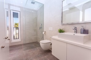 Et moderne badeværelse med en glasbrusekabine, toilet, håndvask med spejl og en lille plante på bordpladen.
