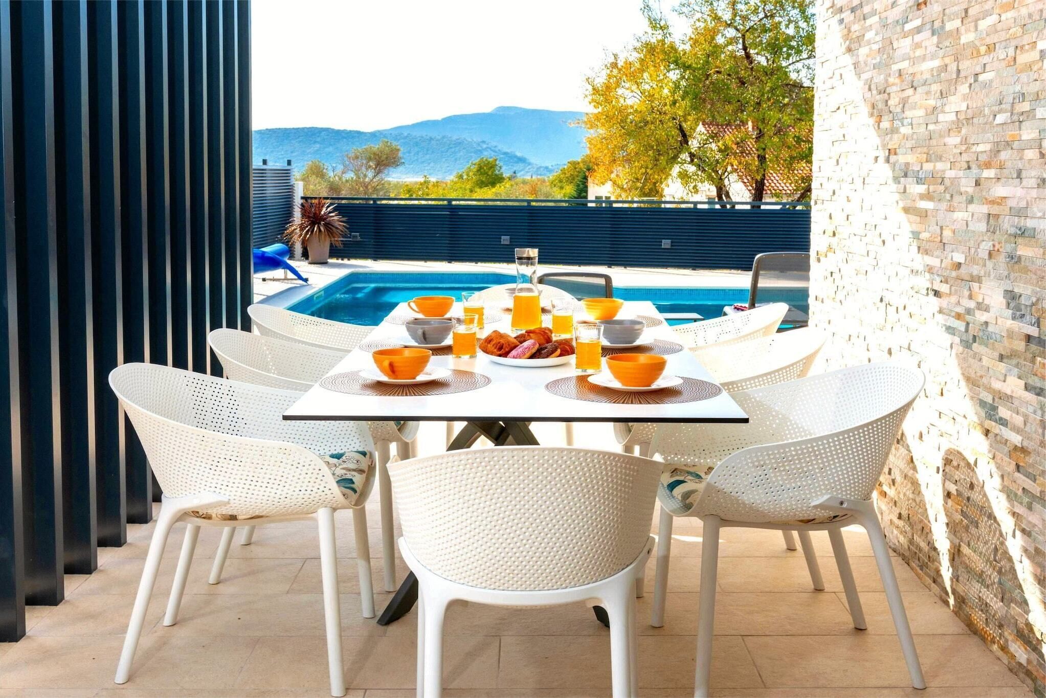 A dining table with chairs and a pool in the background.