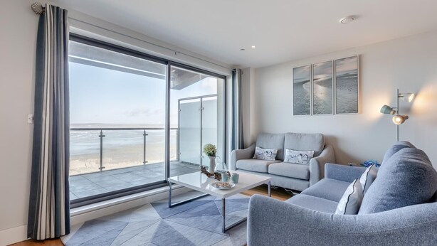 En moderne stue med et stort skydedørsvindue, der fører ud til en balkon med havudsigt.