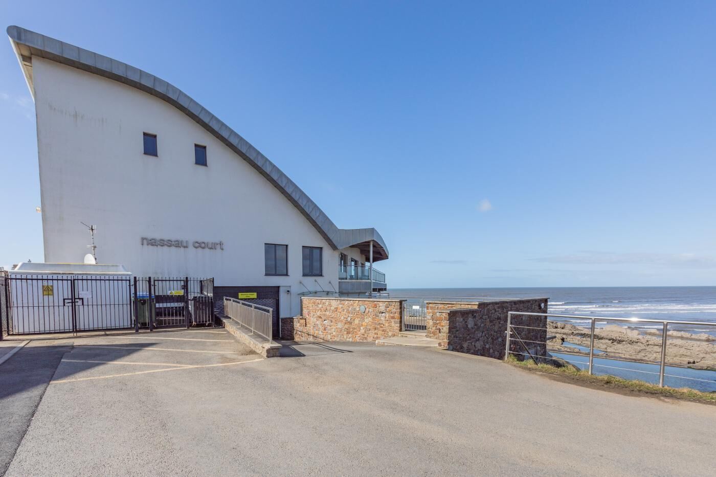 A coastal building with a curved facade, a small balcony, and a view of the sea.