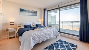 Et moderne soveværelse med en stor seng, udsigt til stranden og en balkon med glasdør.