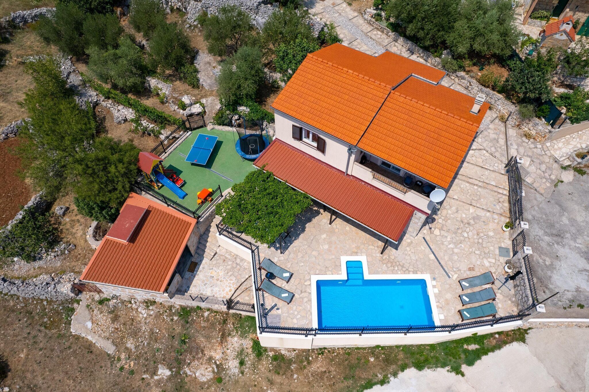 Vista aérea de una propiedad con piscina, cancha de tenis y jardín cercado.