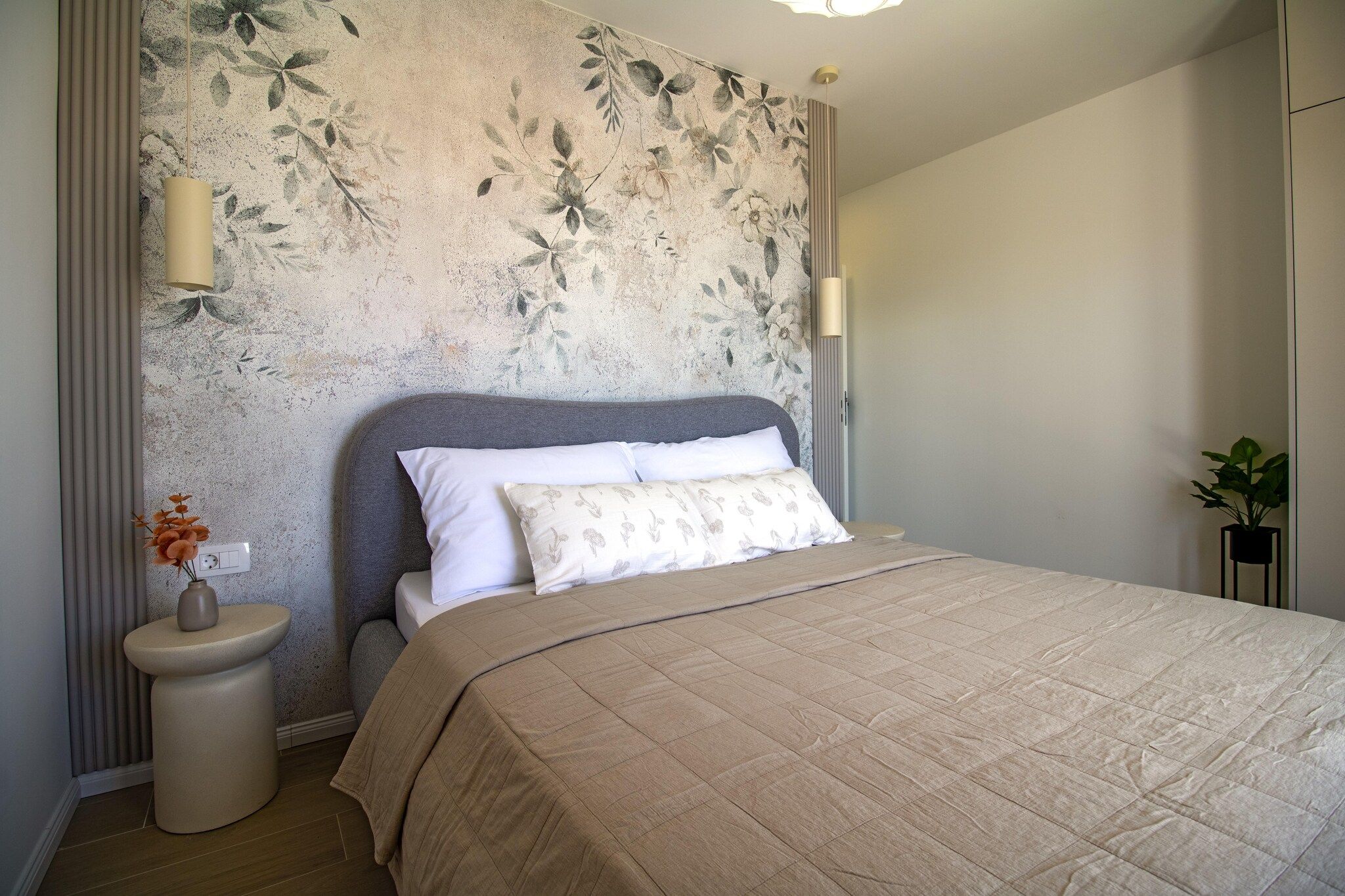 Quarto com cama, luminárias de cabeceira, mesa de cabeceira e planta em vaso.