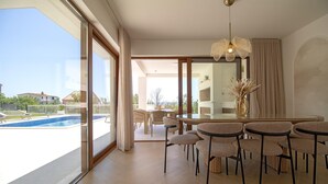 A spacious room with a large window, a dining area with round tables and chairs, and a view of a swimming pool outside. - Beach Villa with pool near Split (Split-Dalmatia County,)