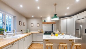 Une cuisine moderne avec des meubles blancs, un plan de travail en bois, un îlot central doté de tabourets, un réfrigérateur en acier inoxydable et une suspension verte.