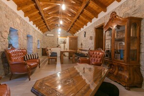 Ein Zimmer mit Steinwänden, Holzbalkendecke, Ledersofas, einem Glastisch und einem Holzschrank mit Glastüren.