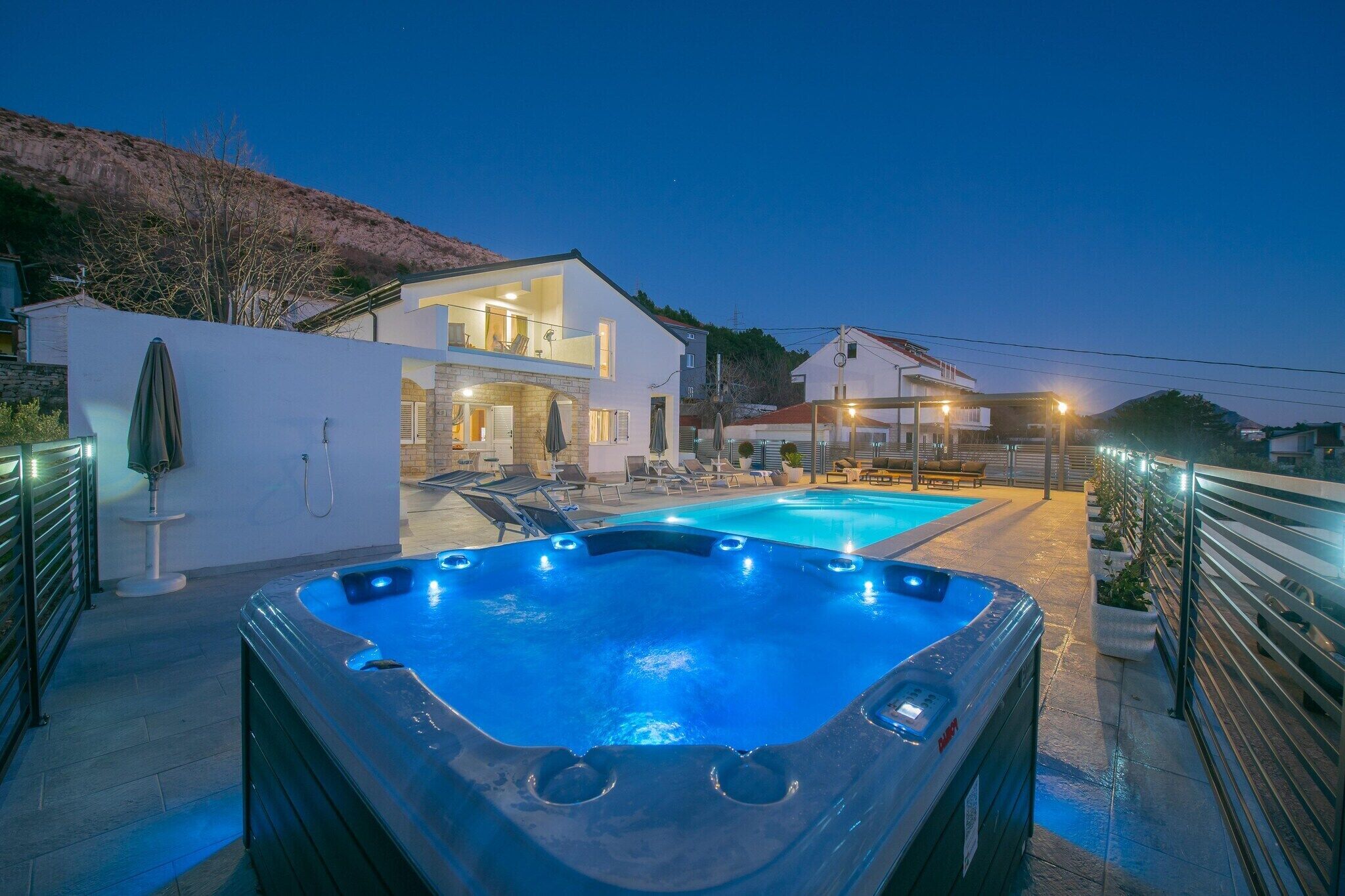 Uma área de piscina moderna ao ar livre, com hidromassagem, espreguiçadeiras e um caminho bem iluminado.