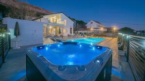 Un área de piscina moderna al aire libre con un jacuzzi, sillones reclinables y un sendero bien iluminado.
