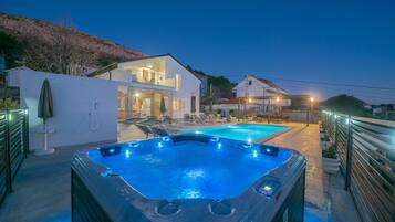 Uma área de piscina moderna ao ar livre, com hidromassagem, espreguiçadeiras e um caminho bem iluminado.