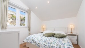 Un dormitorio con una cama, dos mesitas de noche con lámparas, una ventana con cortinas y vistas al exterior.