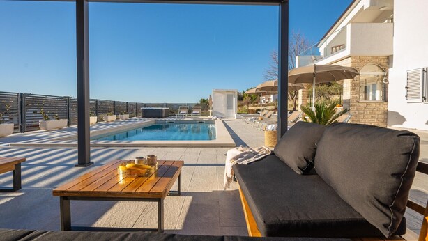 Un área de piscina en la azotea con un sofá, mesa y sillones de descanso.