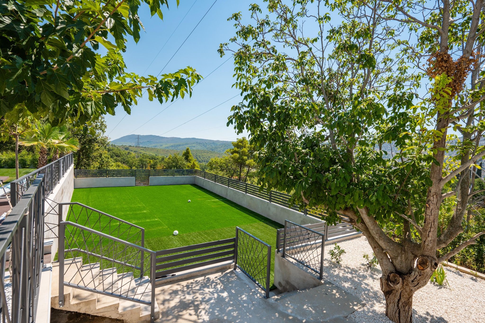 Un césped verde y bien cuidado con un arco de fútbol, rodeado por una valla metálica y escaleras que suben a una plataforma de observación.