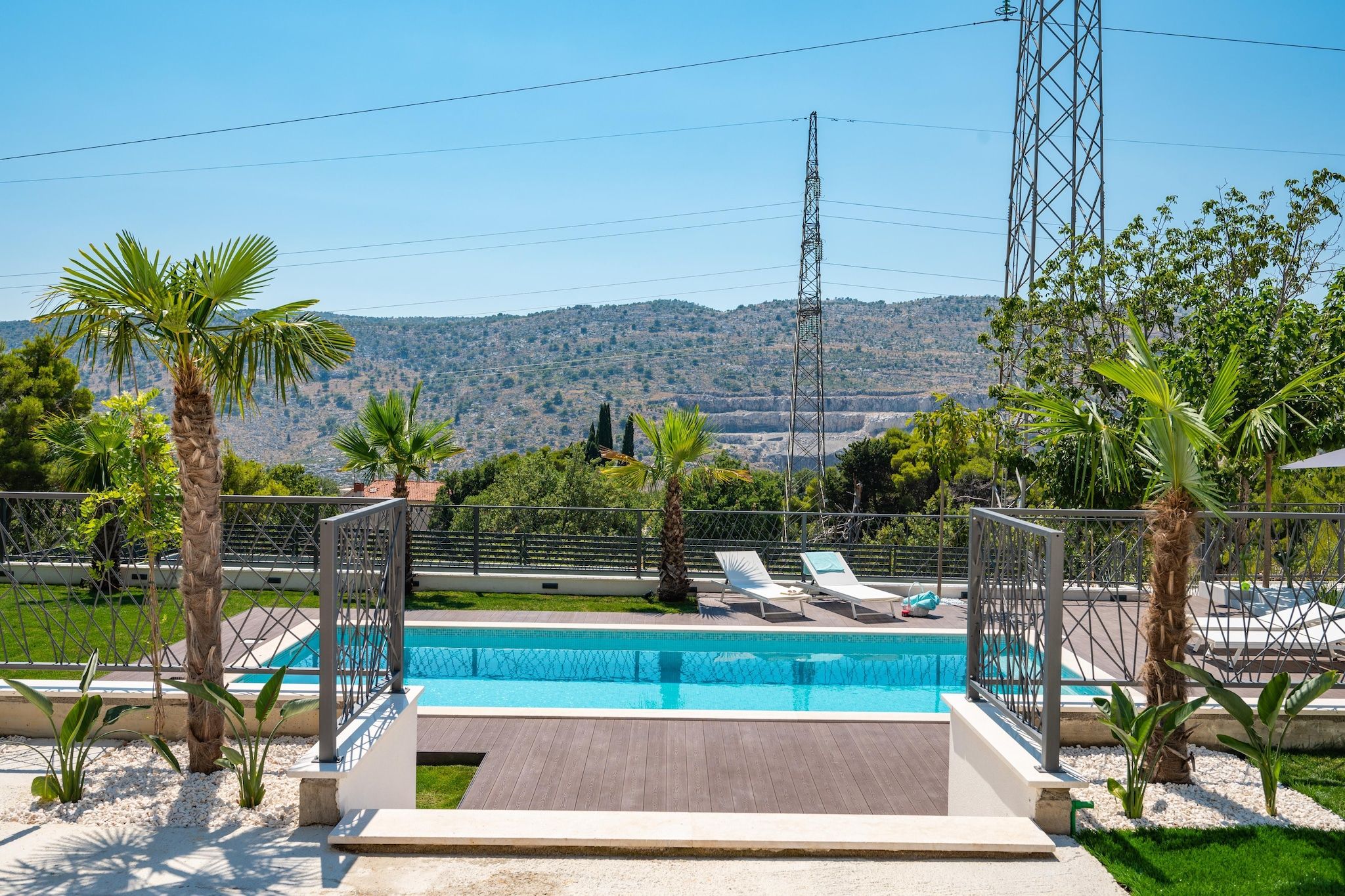 Una piscina con vistas a un paisaje montañoso, rodeada de palmeras y una cerca metálica.