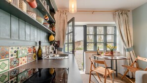 Een keuken met een spoelbak, een eethoek met stoelen en uitzicht door een raam.