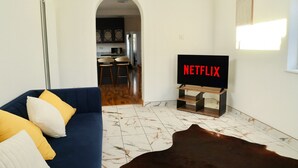 Una sala de estar con un sofá azul, un tapete de piel de vaca y un mueble para televisión con el logotipo de Netflix.