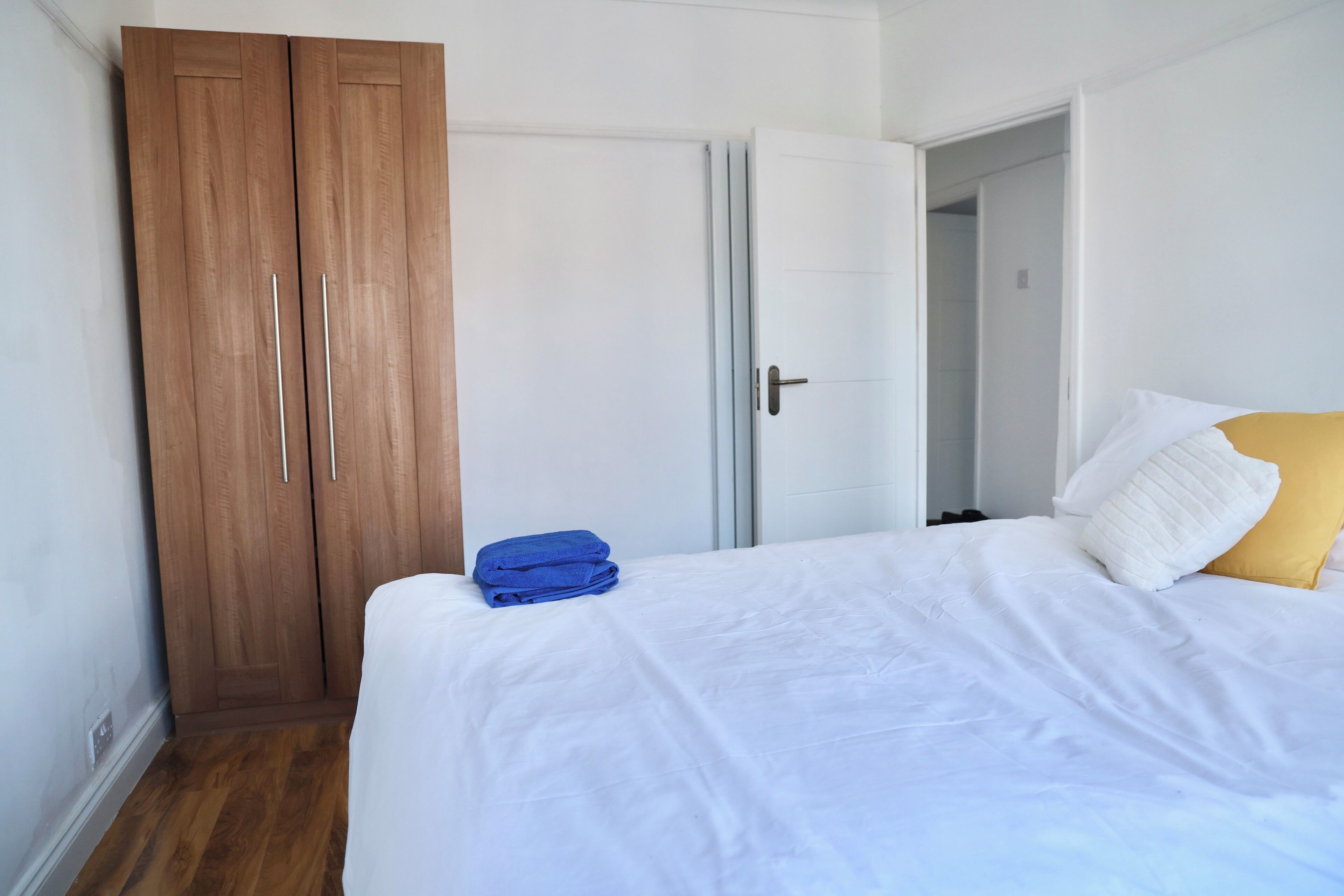 A bedroom with a bed, white bedding, a blue towel, a wooden wardrobe, and a white door.