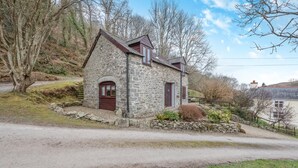 A stone house with a red door and windows, surrounded by a stone wall and a grassy area. - 2 Bed in Llwyndafydd (oc-c31062) (Llandysiliogogo)