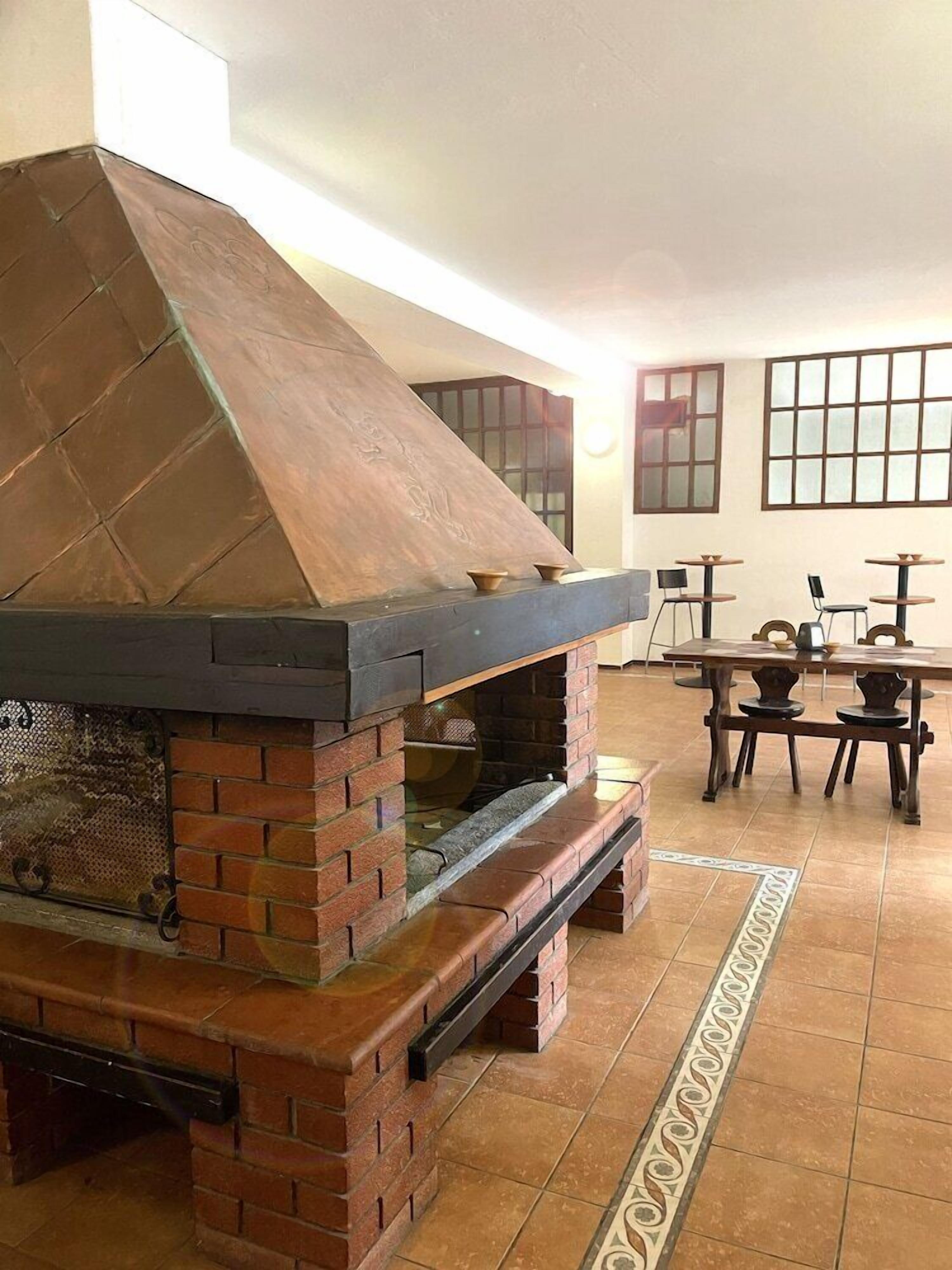 Una cocina al aire libre de ladrillo con chimenea, una zona de comedor con mesas y sillas, y una alfombra estampada en el suelo.