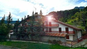 A two-story house with a stone facade, red wooden balcony railings, and a mountainous backdrop. - HOTEL DU SOLEIL (Mongnod)