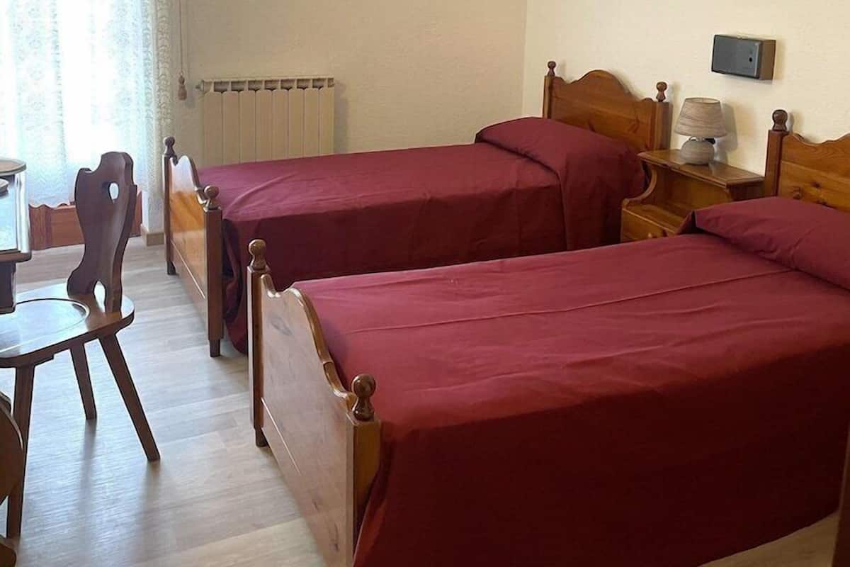 A room with two wooden beds, a wooden chair, a small table, and a radiator.