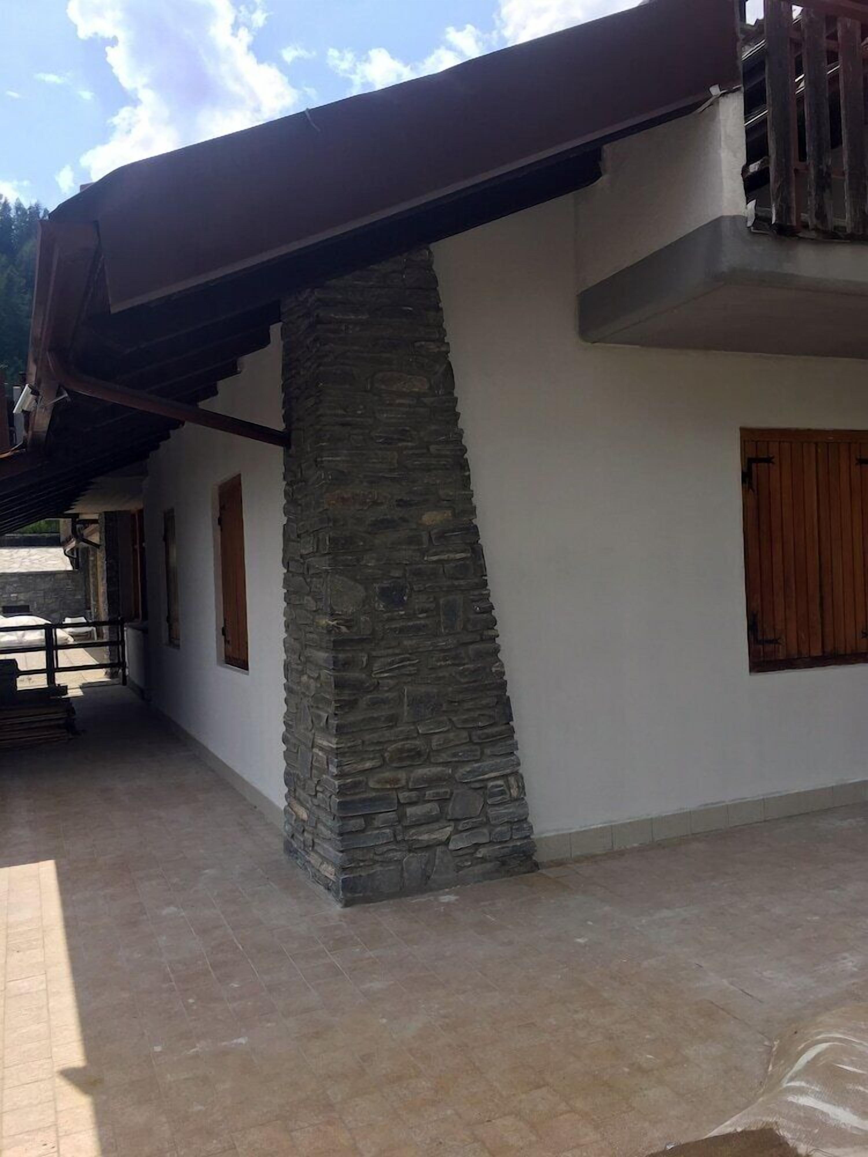 Un edificio con un pilar de piedra, paredes blancas y contraventanas de madera.