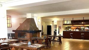 A spacious dining area with wooden tables and benches, a brick fireplace, and a kitchen area with a bar. - HOTEL DU SOLEIL (Mongnod)