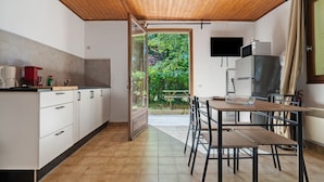 A kitchen with a wooden ceiling, a dining area with a table and chairs, a refrigerator, and a window with a view of greenery. - Holiday Home “Maison 4 Personnes” – Optional AC, Shared Pool (Calviac-en-Périgord)