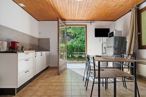 Eine Küche mit Holzboden, ein Essbereich mit Tisch und Stühlen, ein Kühlschrank und ein Fenster mit Blick auf Grünflächen.