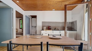 A modern kitchen with a wooden table, chairs, and a view into the adjacent bedroom. - Holiday Home “Maison 4 Personnes” – Optional AC, Shared Pool (Calviac-en-Périgord)