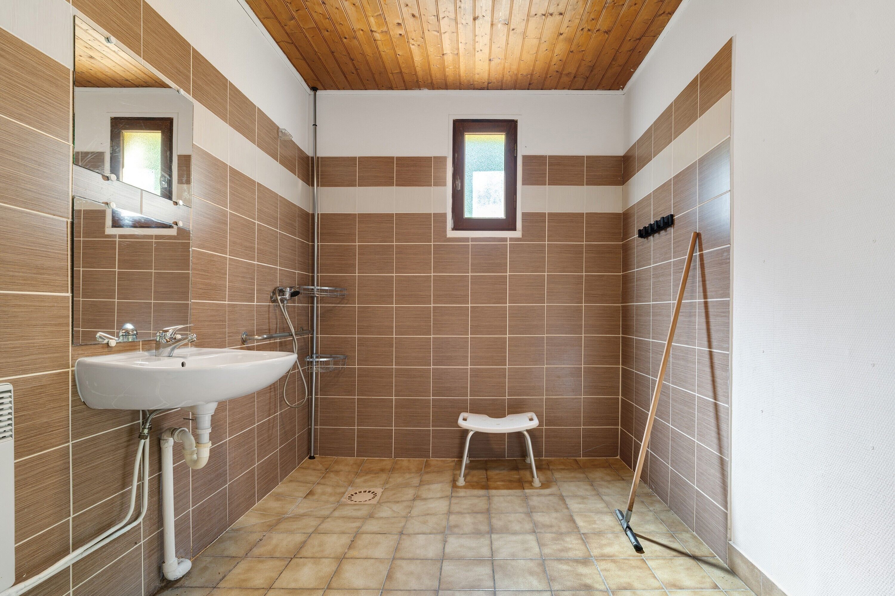 Une salle de bain avec un lavabo, un miroir, une douche et une petite fenêtre.