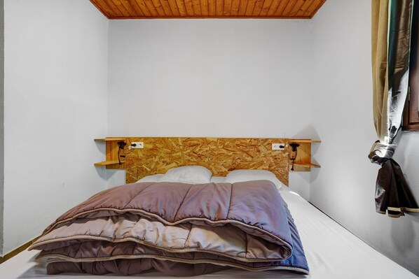 A single bed with a wooden headboard, a brown and purple blanket, and a wooden shelf above the bed.