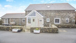 A stone building with a small porch, a bench, and potted plants. - 3 Bed in Llanfwrog (oc-f31053) (Llanfaethlu)