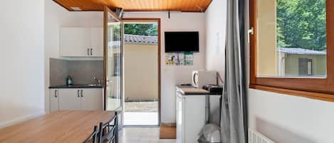 A compact kitchen with a wooden ceiling, a dining table with chairs, a washing machine, and a TV mounted on the wall.