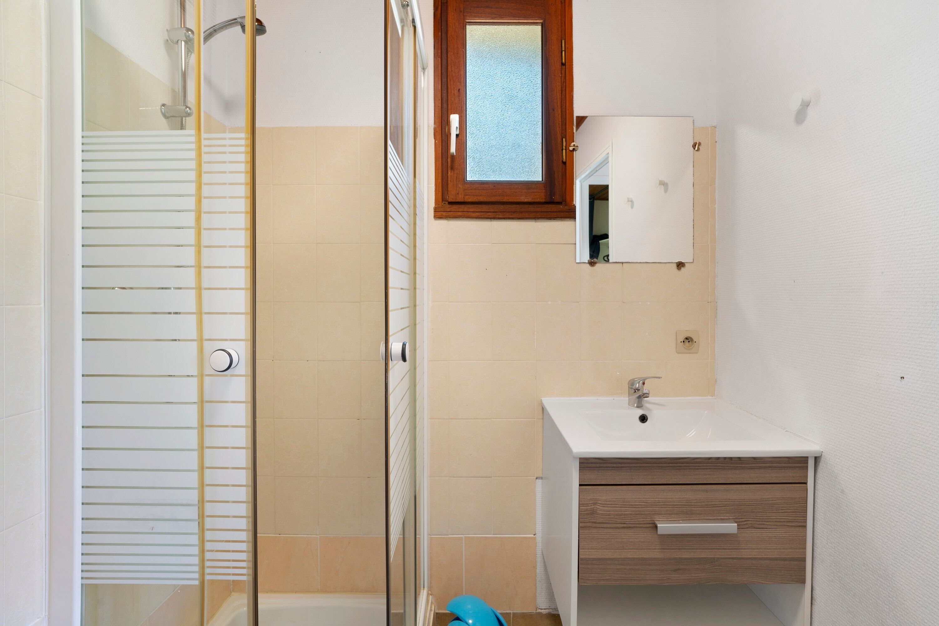 A bathroom with a glass shower enclosure, a white sink with a wooden cabinet, and a mirror above the sink.