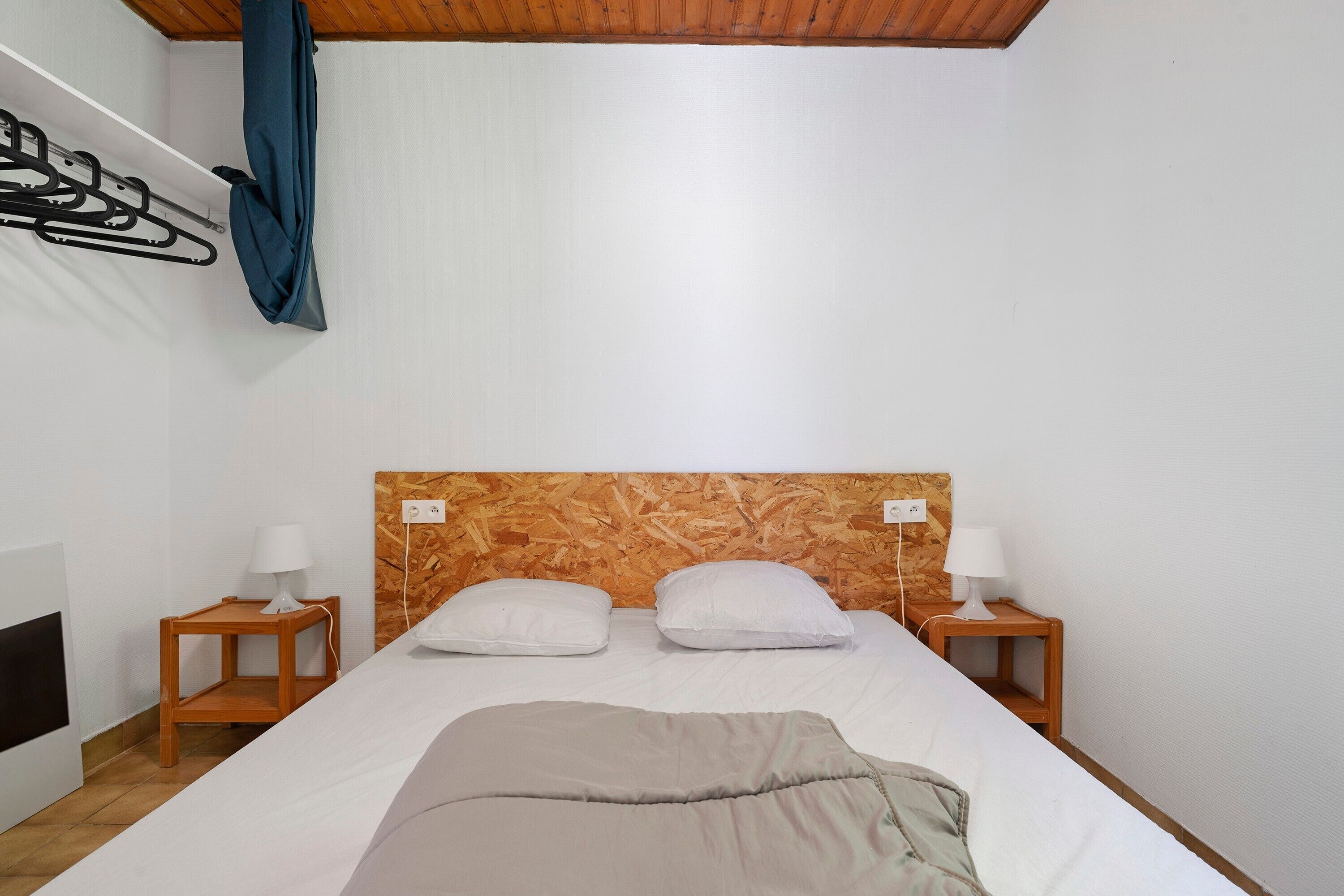 A bedroom with a wooden headboard, two bedside tables with lamps, a bed with white bedding, and a coat hanging on a rack.