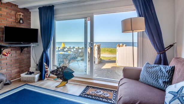 Ein Wohnzimmer mit einer großen Schiebeglastür, die auf eine Terrasse mit Meerblick führt.