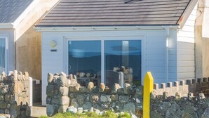 Ein Küstenhaus mit steinverkleideter Eingangspartei, einer Glastür, die zu einer überdachten Veranda führt, und einem grauen Dach.