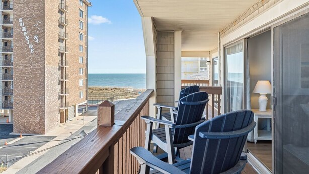 Ein Balkon mit Stühlen und einem Tisch, der auf den Strand blickt, ein Gebäude mit der Aufschrift 'SURFSIDE 84' sowie der Blick auf den Ozean.
