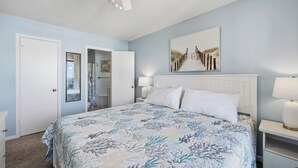 Ein Schlafzimmer mit Bett, Deckenventilator, Nachttisch, Lampe und Tür.