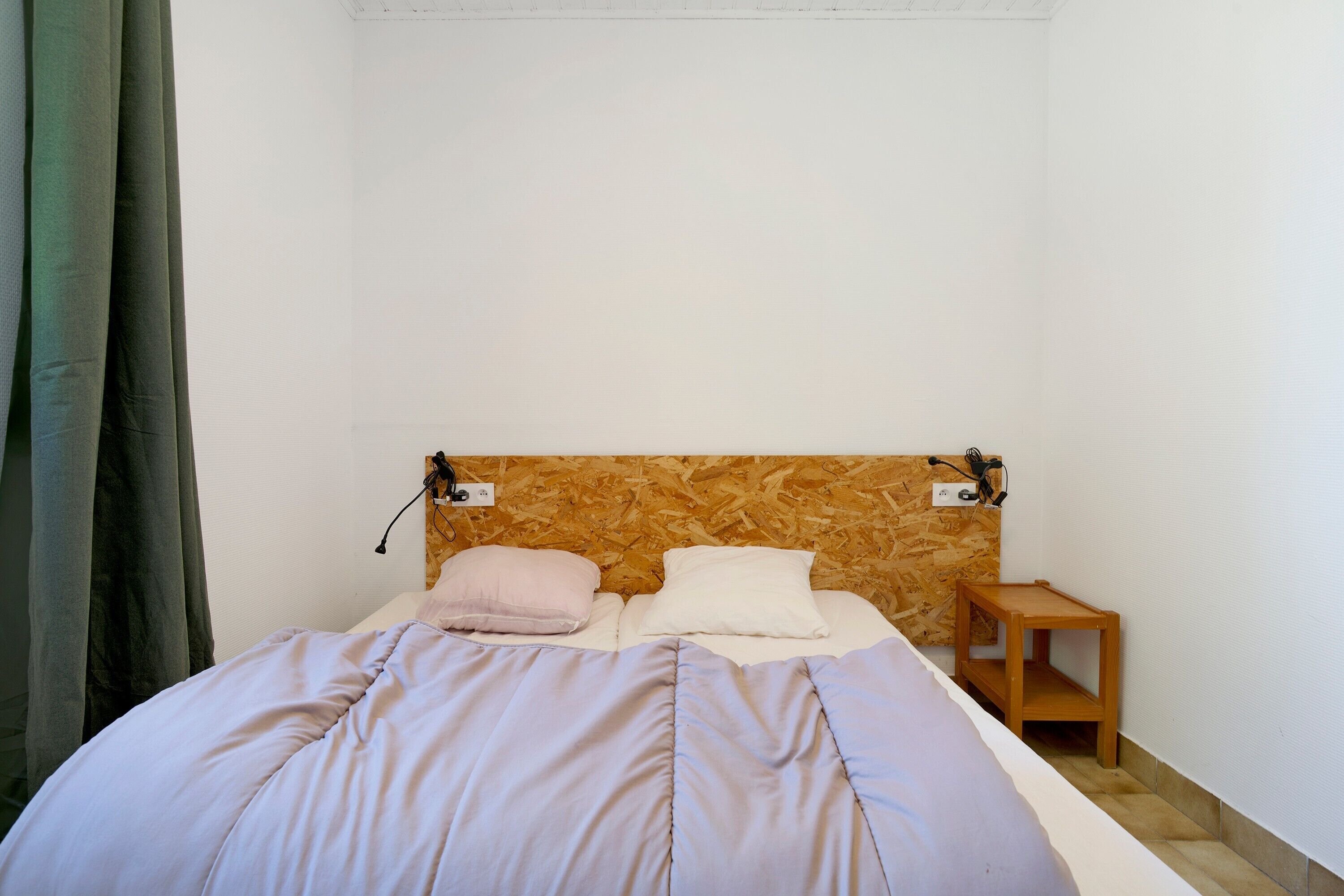 A bed with a wooden headboard, a bedside table, and a curtain.