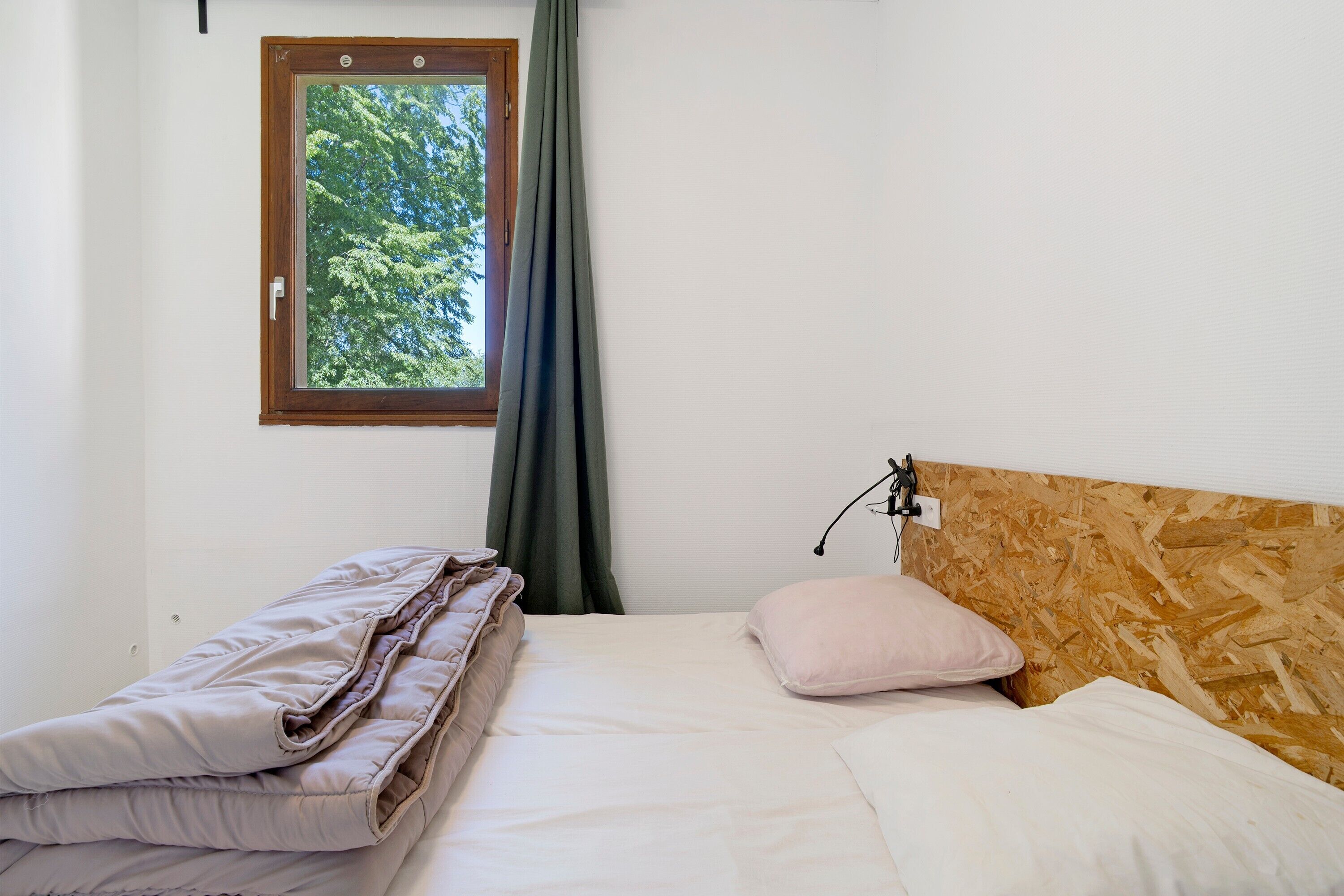 Una camera da letto con una testiera in legno, una finestra vista alberi, un letto con cuscini e un comodino.