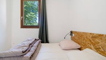 Una camera da letto con una testiera in legno, una finestra vista alberi, un letto con cuscini e un comodino.