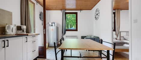 A kitchen with a wooden table and chairs, a refrigerator, and a window with curtains.
