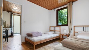 A bedroom with a wooden bed, a window with a view, a bedside table with a lamp, and a bathroom visible through an open door. - Holiday Home 'Maison 4 Personnes' Air Conditioning for Extra Charge Shared Pool (Calviac-en-Périgord)